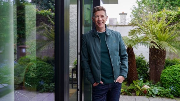 Dermot Bannon leaning against glass door of his house